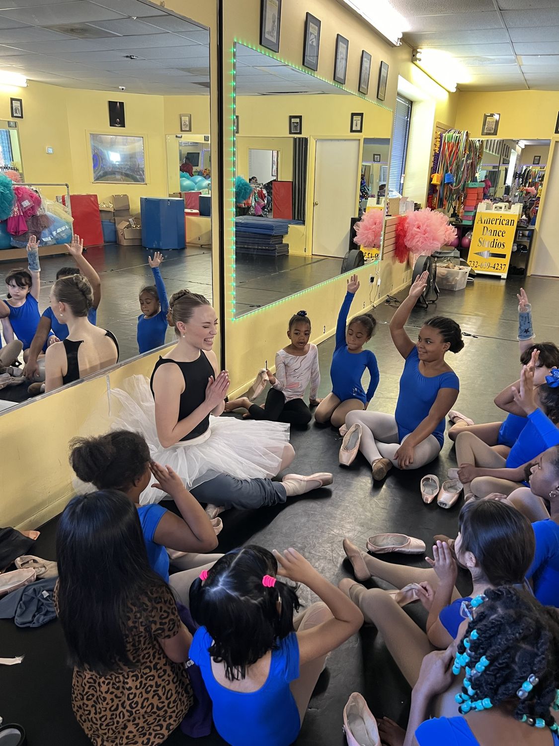 A guest ballerina in a white tutu talking with ADS ballet students sitting in a circle