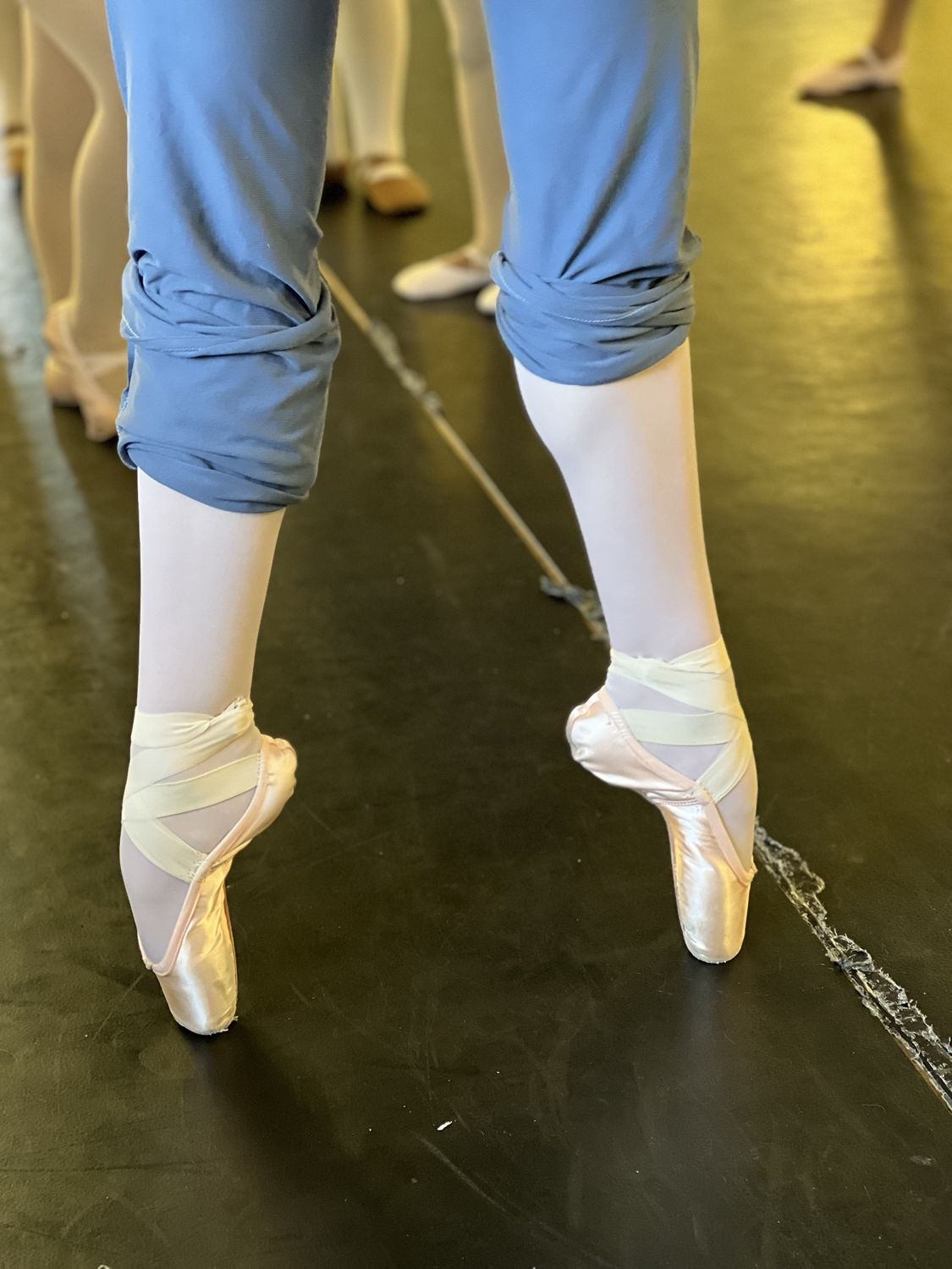 Close-up of an ADS ballet student rising onto pointe in satin pointe shoes