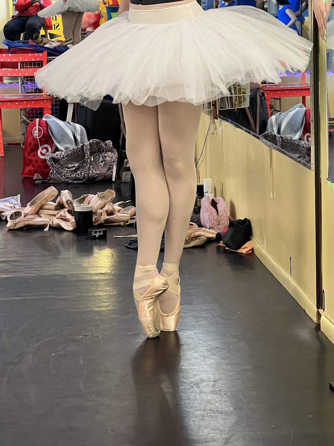 A ballerina in a white practice tutu standing on pointe in the studio