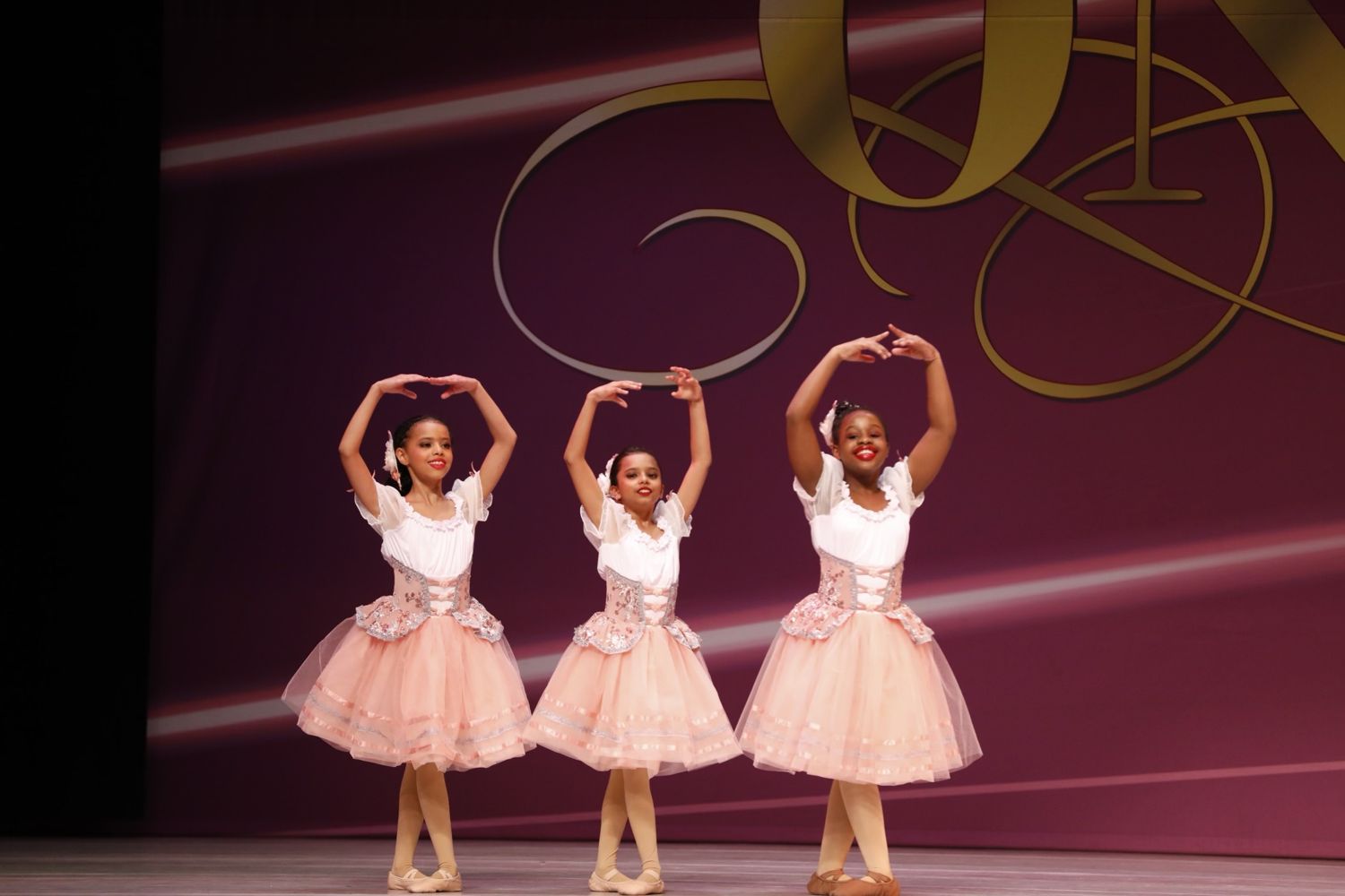 Three ADS ballet students in peach romantic tutus performing on stage with arms in fifth position