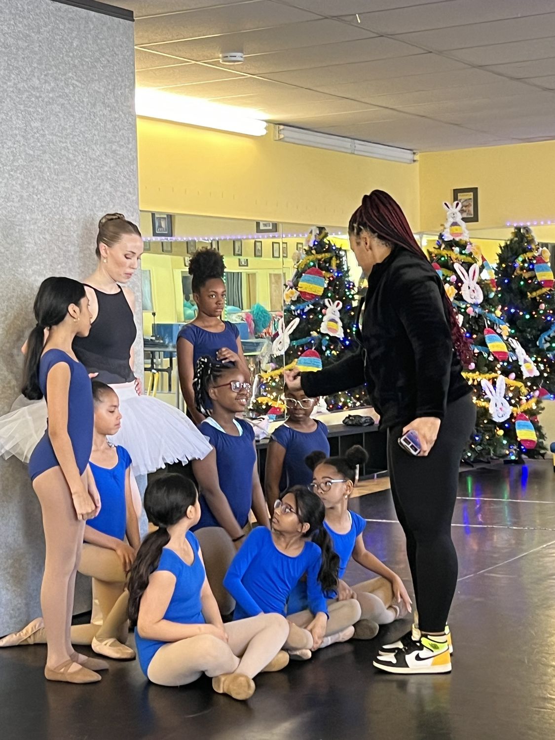 Ballet students in blue leotards gathered with their teacher and a guest ballerina during a ballet workshop