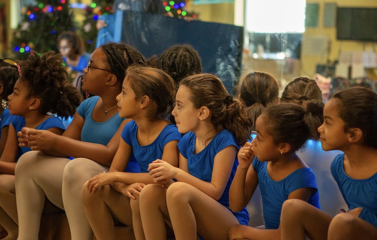 Dancers sitting together and listening during the signature programming portion of class