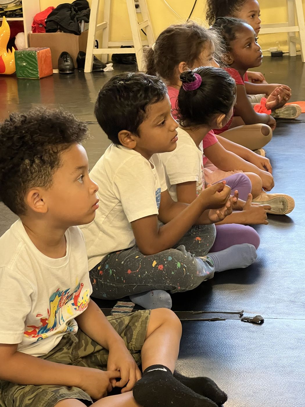 Young boys and girls sitting in a row listening to their teacher