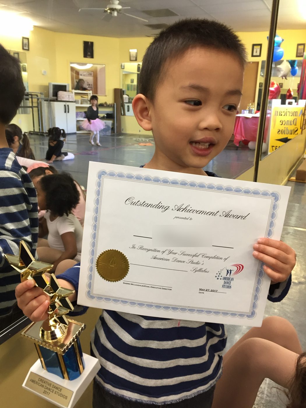 A young boy proudly holding his Outstanding Achievement Award certificate and star trophy