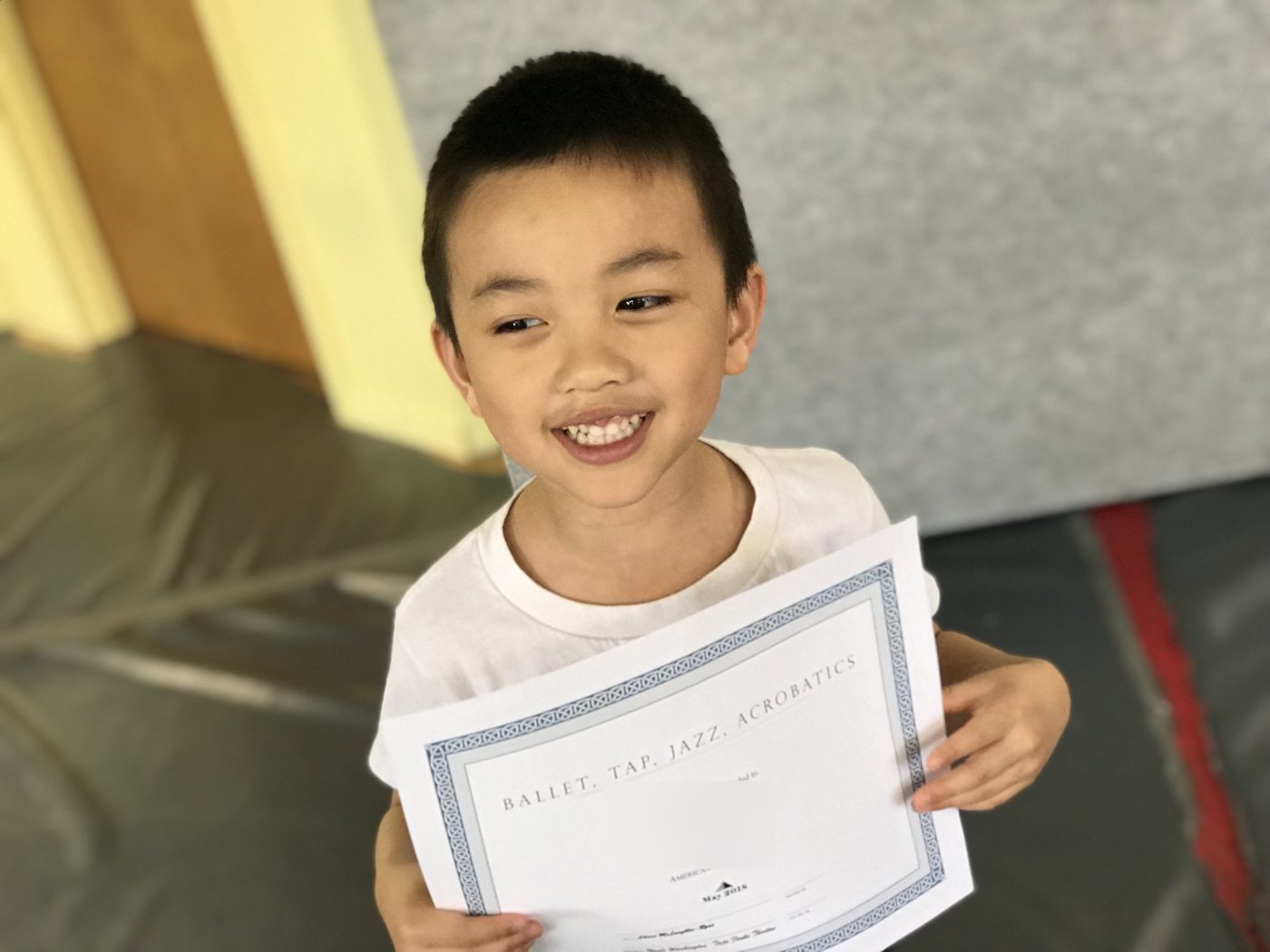 A smiling boy holding his Ballet, Tap, Jazz, Acrobatics syllabus certificate