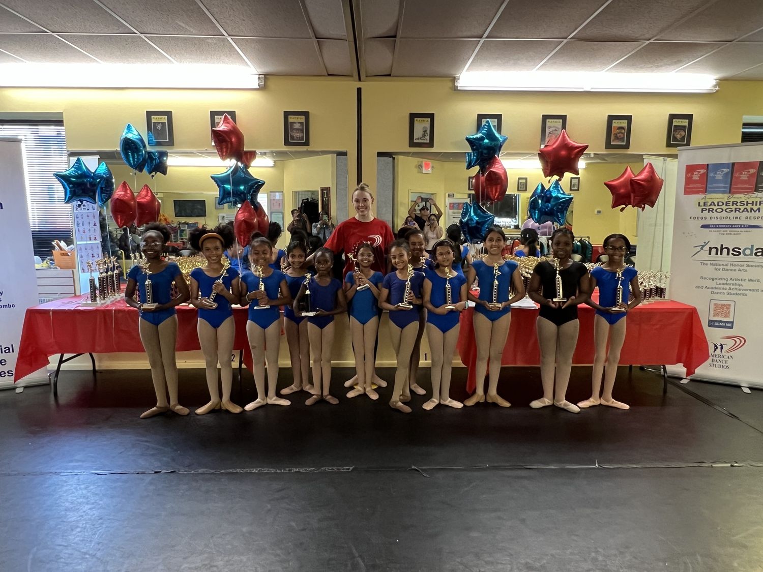 A ballet class holding their graduation trophies with their teacher at the ADS Rise Graduation