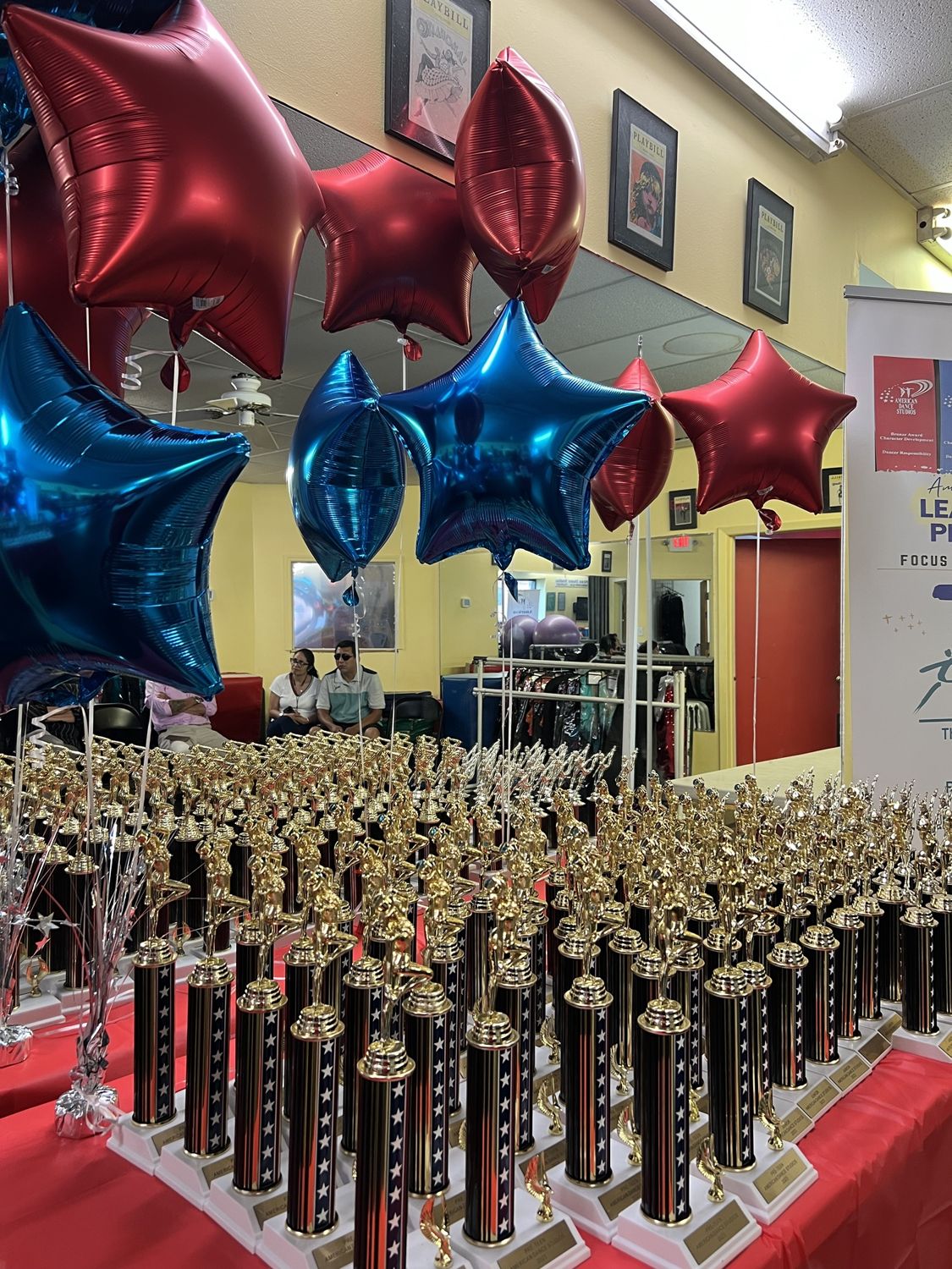 Rows of gold graduation trophies under red and blue star balloons