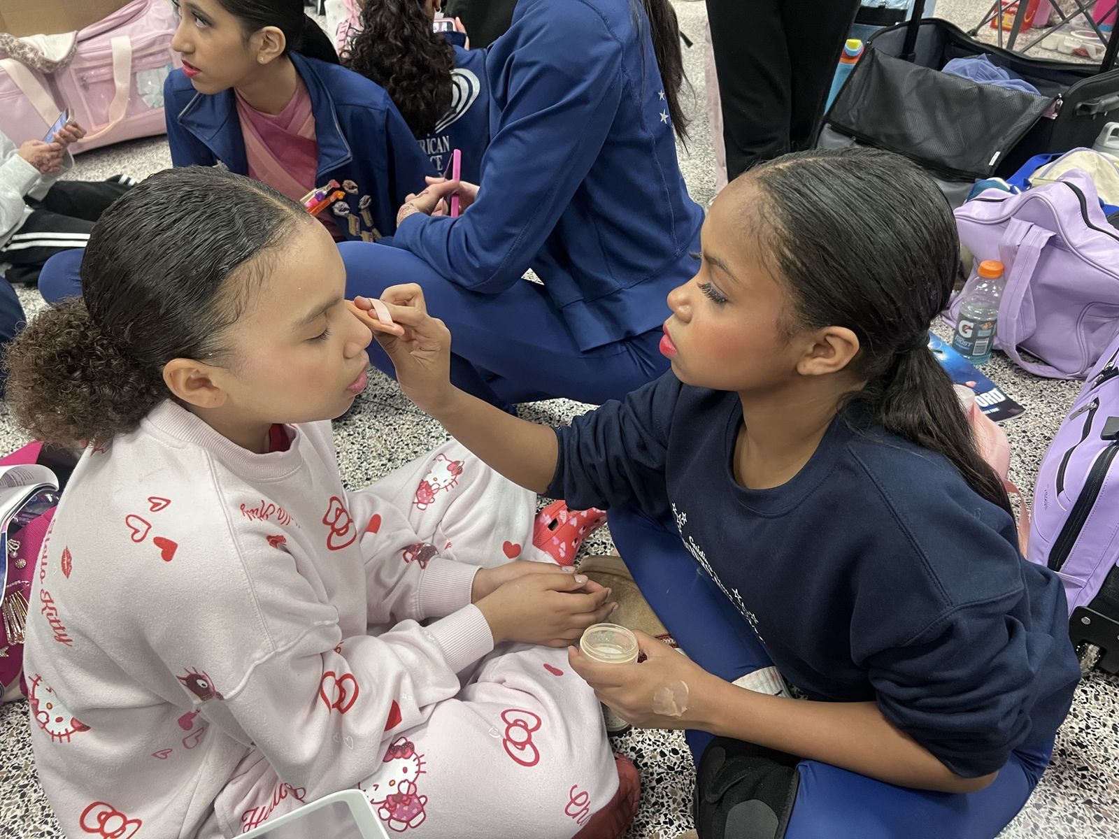 A Guiding Star applying stage makeup to a younger dancer backstage