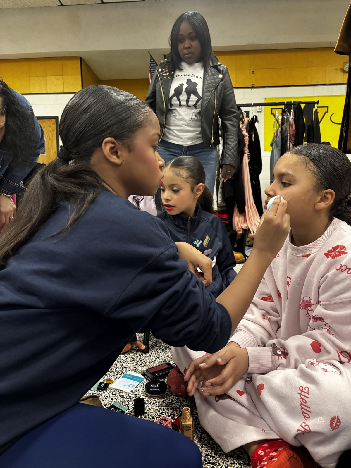 A teacher assistant helping a dancer with makeup backstage