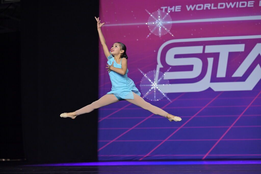 A young dancer in a high split leap on stage