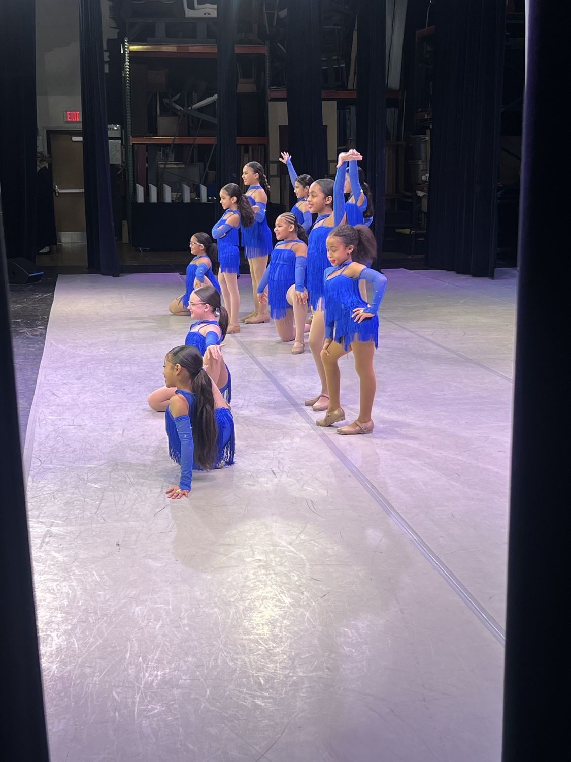 Tap dancers in royal blue fringe costumes holding their pose on stage