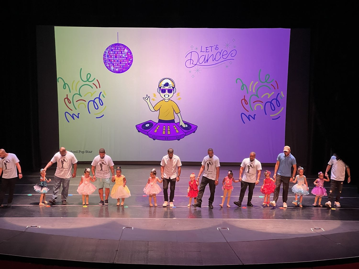 Dads dancing hand in hand with their little daughters on stage in a special father-daughter number