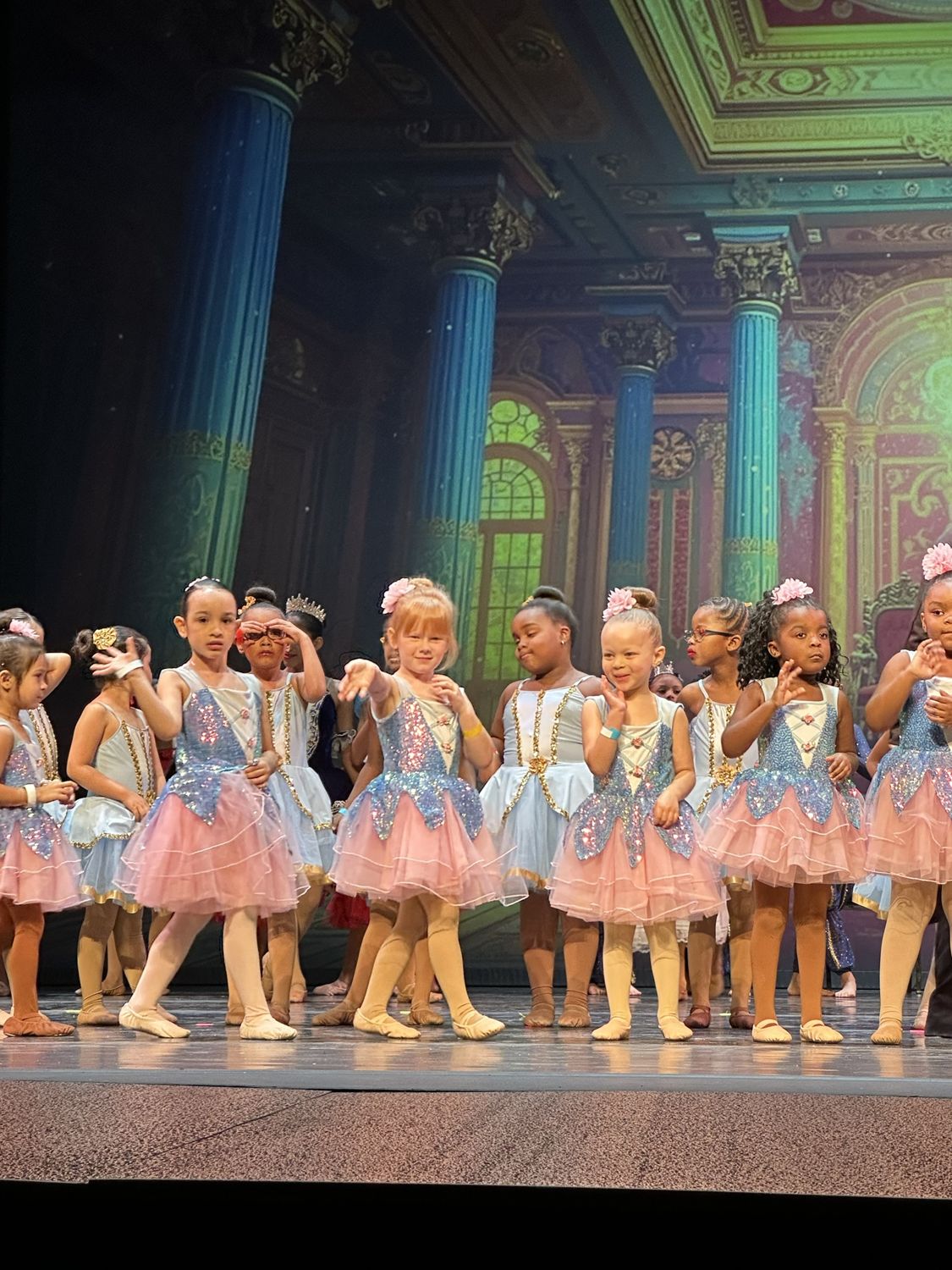 Young ballet dancers in pink and blue costumes on stage at the finale