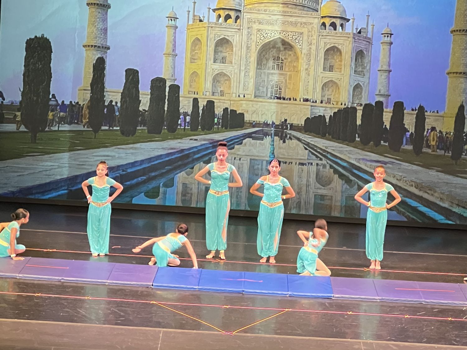 Acrobatics dancers in turquoise costumes performing in front of a Taj Mahal backdrop