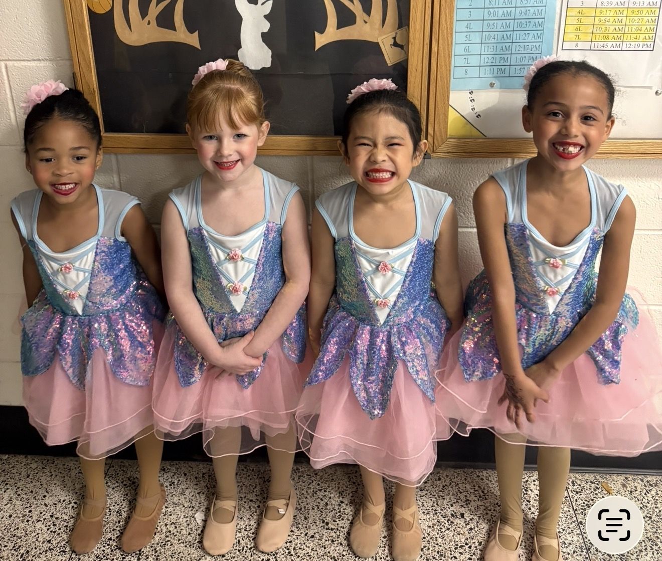 Four little ballerinas in blue and pink sequin costumes smiling backstage