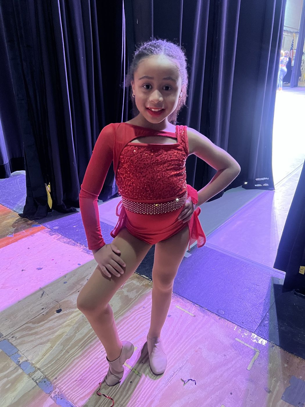 A young dancer in a red sequined costume before her solo
