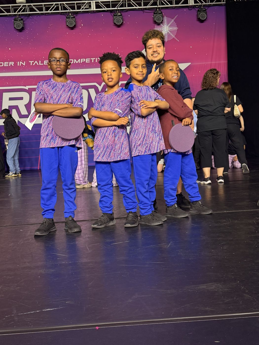 Rhythm Crew boys in matching team shirts on stage with their award plaques and teacher