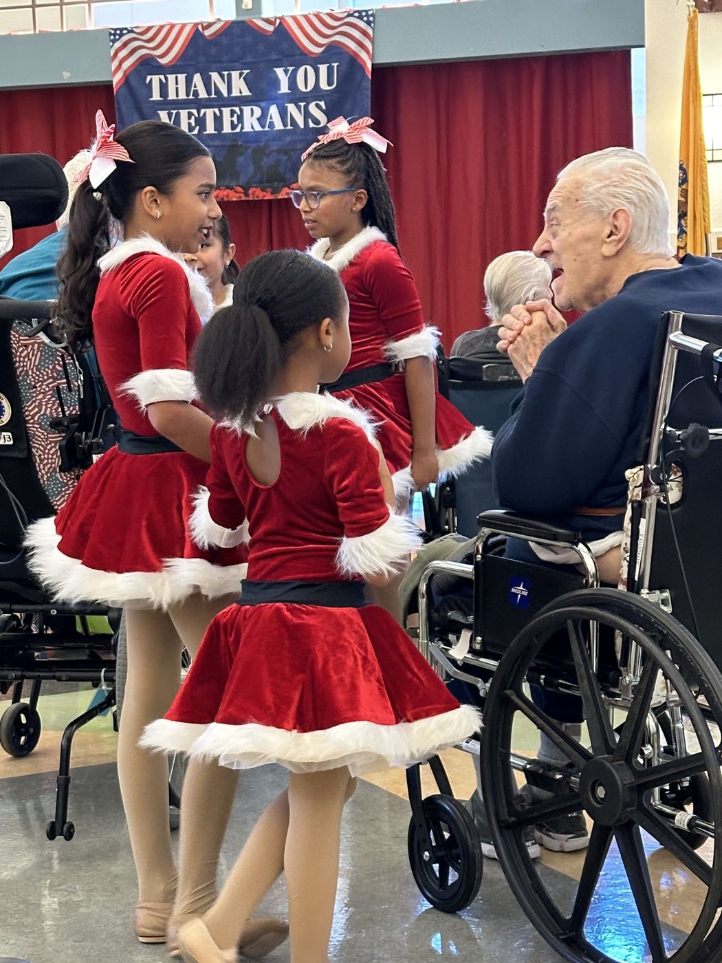 Young dancers in red velvet holiday costumes talking with a smiling veteran